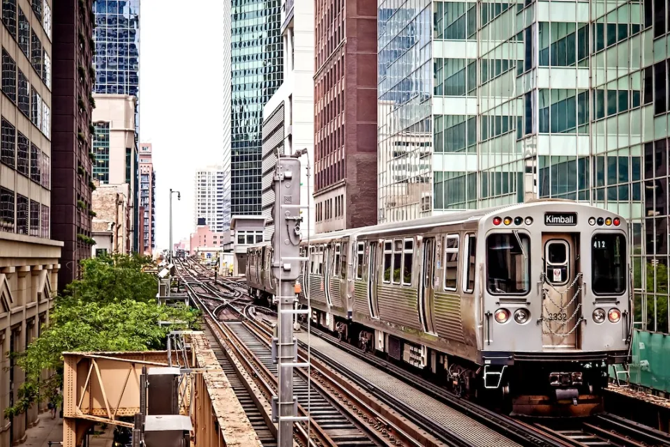 Silver Chicago train passing by dense high-rise buildings on elevated track.